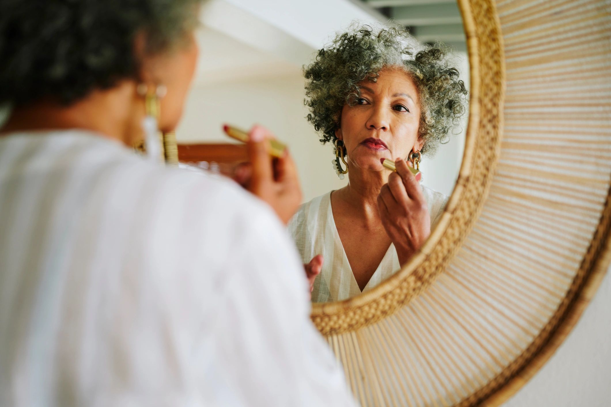 Mature woman putting on lipstick in a mirror at home